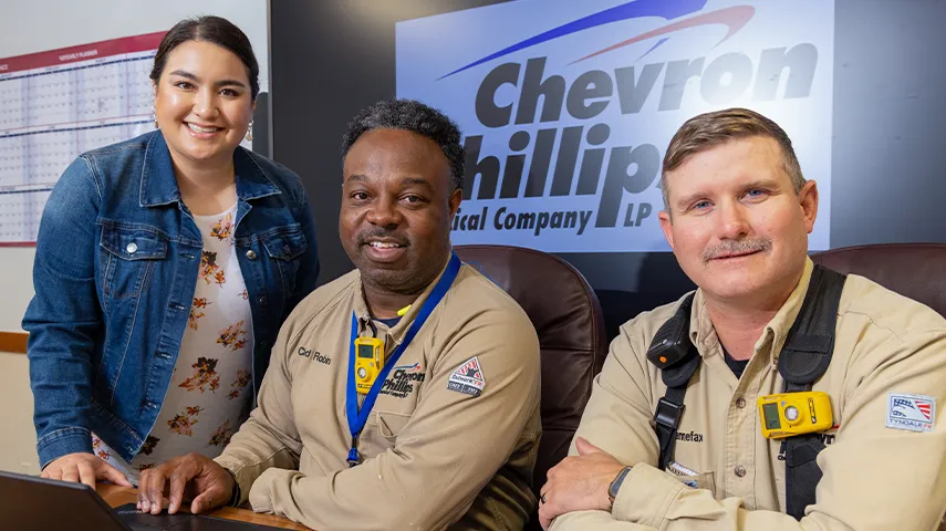 Two employees who wear working clothes sit and one is standing next to them. (Photo)