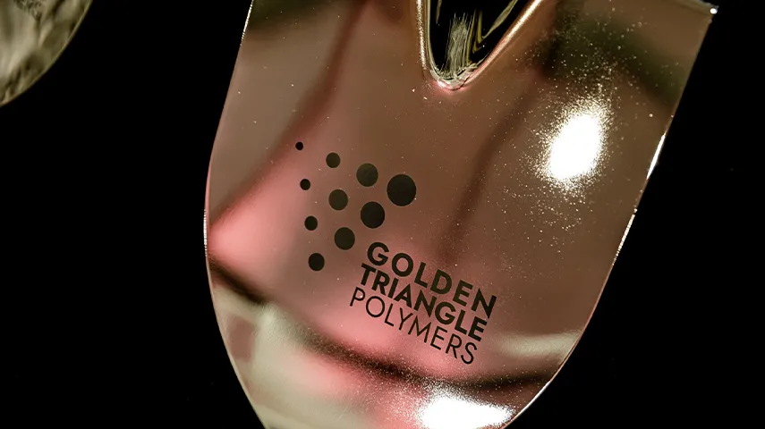 A close up of a golden piece of metal with the text Golden Triangle Polymers (Photo)