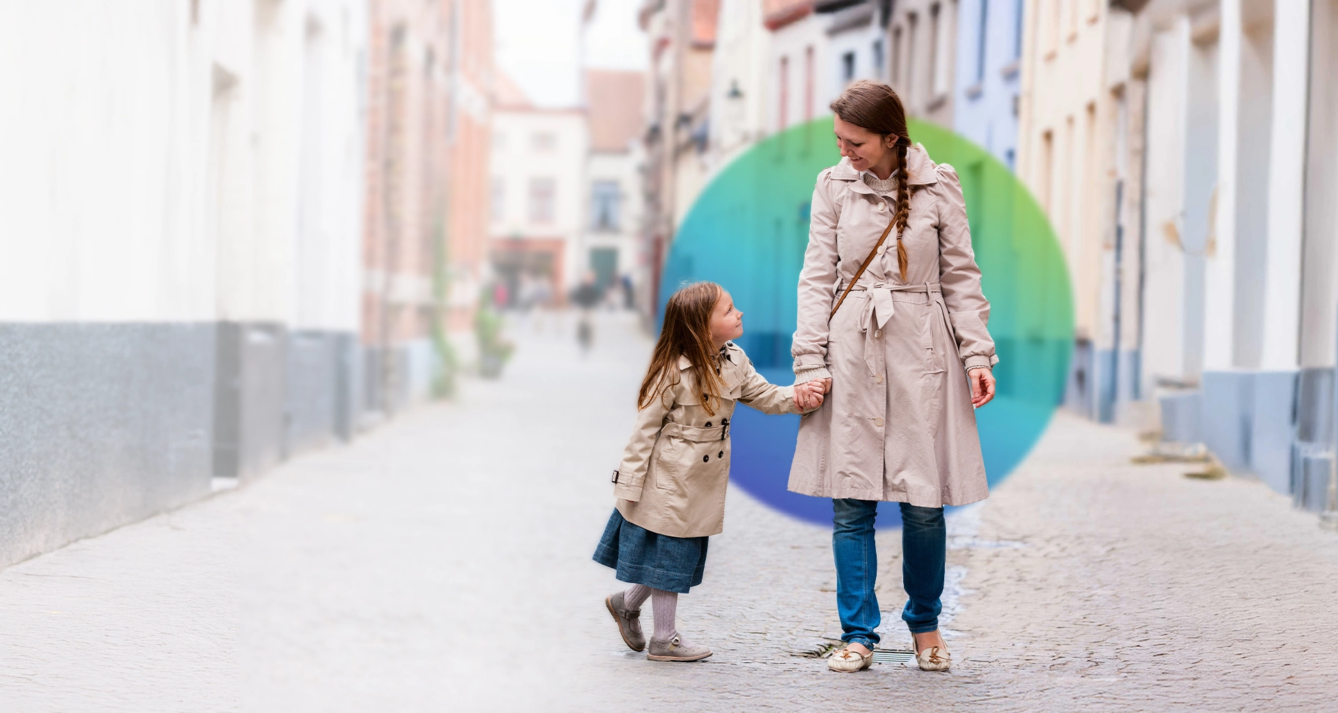 This image shows a woman and a child standing on what appears to be an old, cobblestone street. The woman is wearing a long coat and is holding the hand of the child, who also has a coat. They are both looking towards the same point, possibly engaging in conversation or observing something. In the background, there is a line of old buildings under clear sky, suggesting this photo may have been taken during daylight hours with good weather.