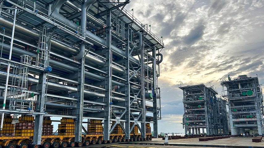 This is an image of a large modern industrial plant. It features a multi-story structure with metal pipes and tanks, under what appears to be a weather system as indicated by the cloudy sky.
