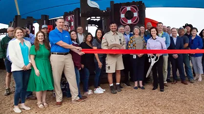 This is an image of a group of people gathered at the grand opening ceremony of a new business or attraction.
The ribbon cutting ceremony is the focal point of the gathering, as indicated by the cut red ribbon across the entrance which signifies the official opening.