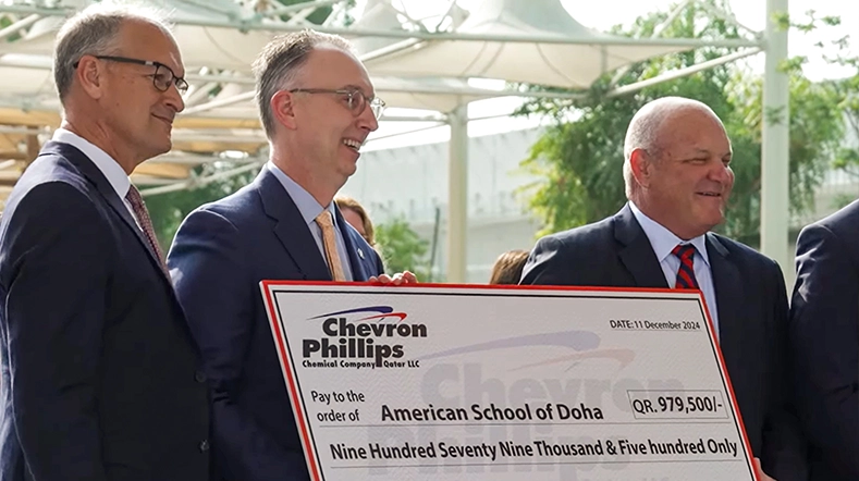 This is an image of a check presentation event. In the center, there is a large check being presented to two individuals standing next to each other. One of them appears to be receiving the check, while the other could possibly be presenting it.