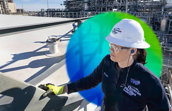
This image shows an individual wearing safety gear who appears to be involved in some kind of construction or maintenance work. The person is standing on a roof, looking down at what might be a new roofing material or some task related to the roofing project. The person is also wearing a vest and has a headset with a microphone on their helmet, which suggests they may be in communication with others on the site or via other workers who might be out of view.