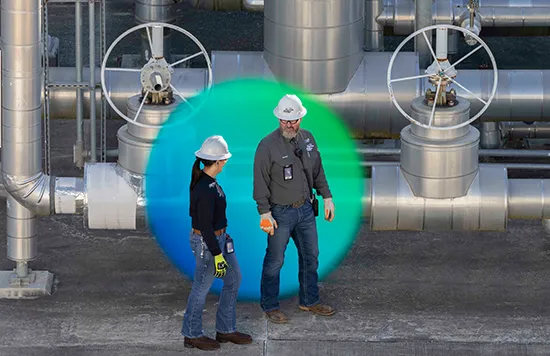 The image shows two individuals in a gas processing or refining facility.
