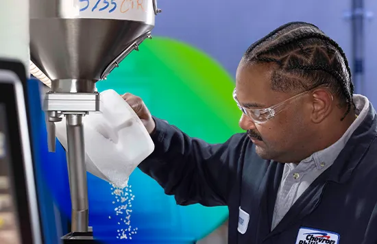 The image shows a person inside what appears to be a small room used for food processing or packaging. They are looking down at some substance in their hands, which looks like bright green flakes or shavings of some kind, possibly ingredients being prepared or processed for use elsewhere in the process.