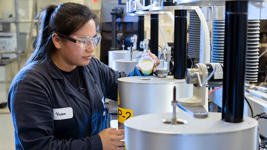 A uniformed woman in a lab pouring some chamicals into a machine. (Photo)