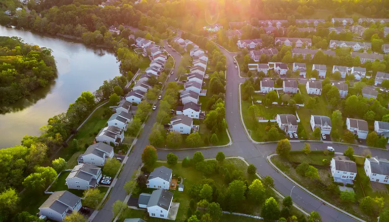 Aerial view of a suburban neighborhood with many houses, trees, and a river (Photo)