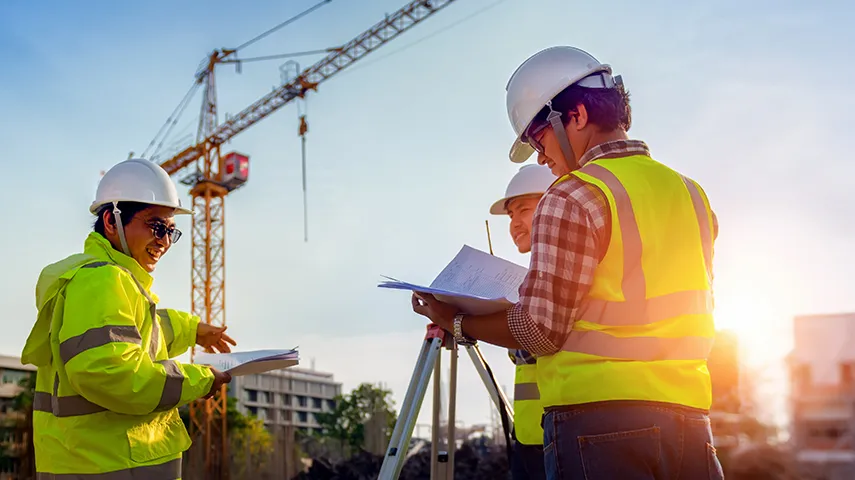 Three people with helmets and safety vests discussing some paperwork at a construction site (Photo)