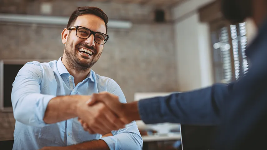 A laughing man shaking hands with another person in an office environment (Photo)