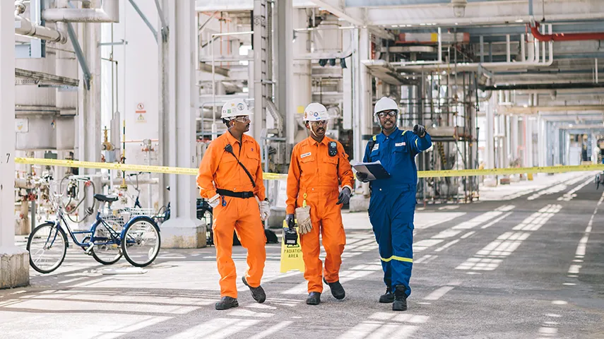 Three workers in overalls with helmets walking through a production site (Photo)